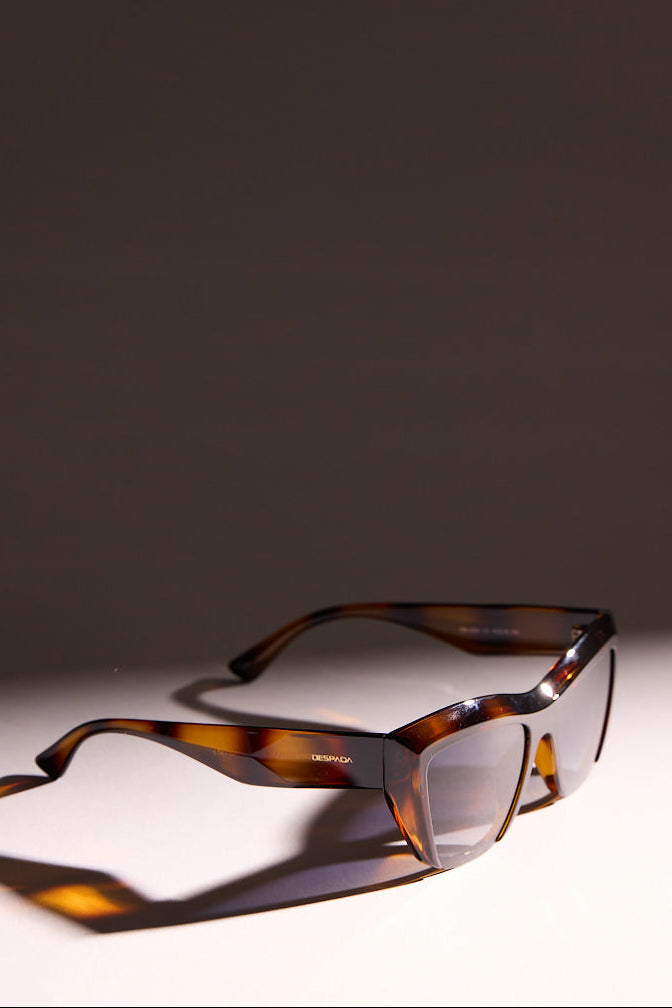 Brown tortoiseshell sunglasses on a reflective surface with a dark background
